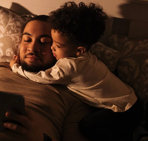 Father and young child sharing an intimate moment on a cozy bed, with warm lighting creating a comforting and peaceful atmosphere.